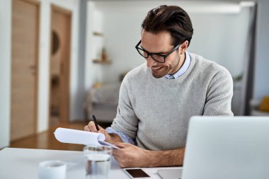 Happy businessman writing notes while working on a computer at home. 