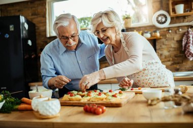 Happy mature woman enjoying with her husband while preparing bruschetta in the kitchen. 