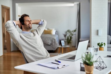 Young happy entrepreneur relaxing with hands behind head after working on a computer at home.