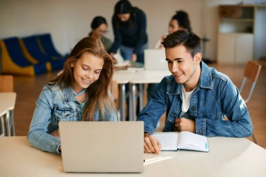 Happy high school classmates using laptop while learning during a class in the classroom. 