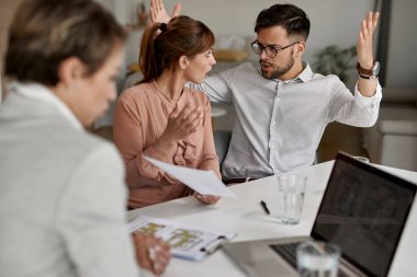 Young displeased couple arguing while having a meeting with real estate agent. 