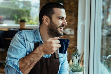 Young happy man drinking coffee and looking through the window. 