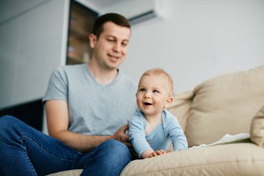 Cute baby boy crawling on the sofa while spending time with his father at home.