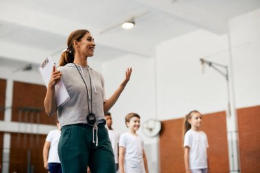 Young happy physical education teacher talking during a class at school gym. 