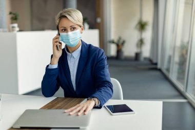 İş kadını, koronavirüs salgını sırasında ofiste maske takarken bir telefon görüşmesi yapıyor.. 