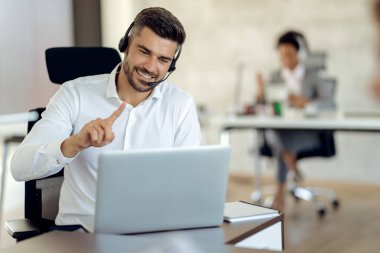 Happy businessman wearing headset and making video call over laptop while working in the office. 