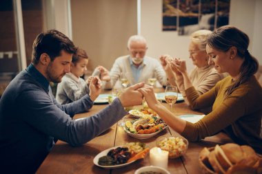 Grateful extended family saying grace while sitting at dining table and holding hands. 