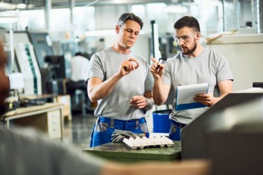 Industrial workers cooperating while doing quality control of manufactured products in a factory. 
