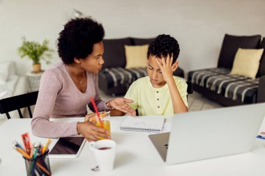 Black mother communicating with her son while assisting him in homework. 
