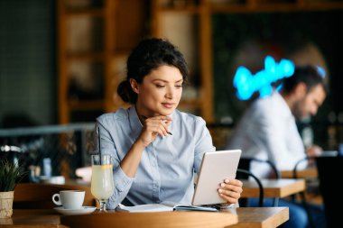 Young businesswoman surfing the net on touchpad while sitting in a cafe.