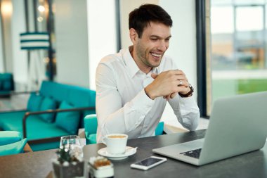 Happy businessman using laptop while having coffee break in a cafe. 