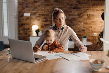 Single mother analyzing paperwork and working while being with her son at home.
