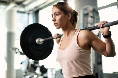 Young athletic woman exercising with barbell during weight training in a gym.