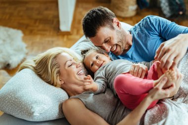 Young happy parents having fun with their small daughter while relaxing on the bed. 