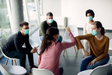 Group therapy participants elbow bumping and wearing face masks due to coronavirus pandemic. 