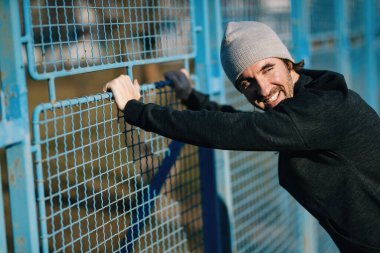 Young happy athlete taking a break from exercising and leaning on a fence outdoors.