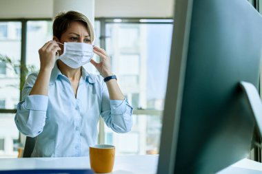 Young businesswoman using protective face mask while preparing for work in the office. 