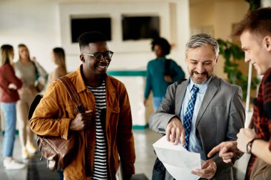 Happy teacher and his students going through exam results while standing in a lobby.  
