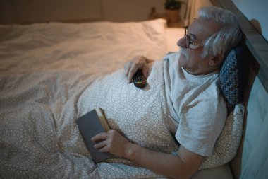 Gülümseyen olgun bir adam yatağa uzanıp gece televizyon izliyor.. 