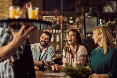 Happy woman and her friends communicating with a waiter and having fun in a pub. 