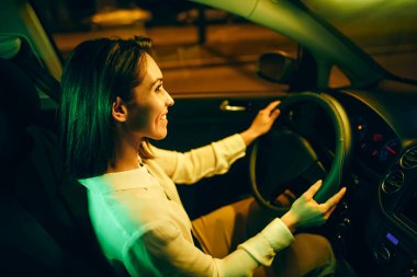 Genç, mutlu bir kadın araba kullanıyor ve şehirde gece gezintisinin tadını çıkarıyor.. 