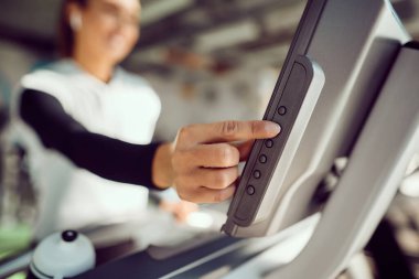 Close-up of sportswoman adjusting speed while running on treadmill in a gym.