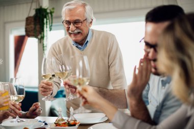 Cheerful senior man and his family toasting during lunch at dining table. 