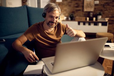 Happy man showing thumb up while having video call over laptop and working at night at home. 