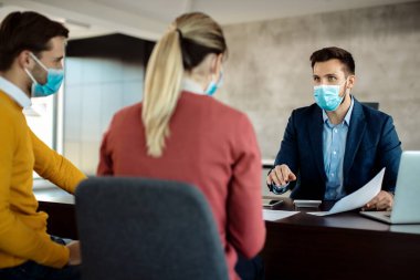 Financial consultant communicating with a couple and wearing face mask during the meeting due to coronavirus pandemic. 