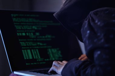 Unrecognizable computer hacker programming software while stealing data on a computer.