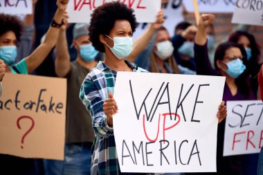 African American woman holding a placard with wake up America inscription while being on a protest against coronavirus measures and restrictions. 