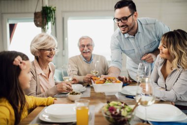 Happy man serving food at dining table while having lunch with his family at home. 