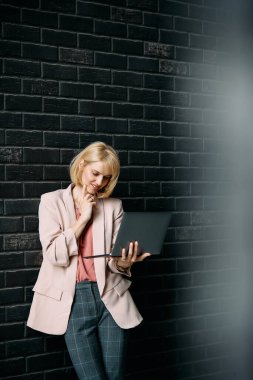Smiling businesswoman reading surfing the net on laptop against the wall. Copy space.