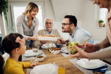 Happy man smelling food while his wife is serving lunch to their family at dining table. 