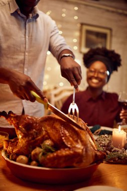 Close-up of African American man carving traditional turkey meat during Thanksgiving lunch at home, 
