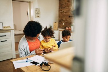 African American mother talking to her daughter while working at home. Small boy is sitting beside them. Copy space. 