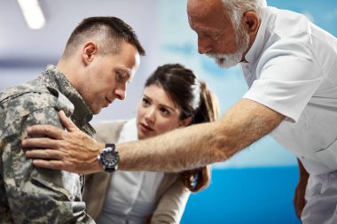 Senior doctor consoling distraught soldier who came to medical appointment with his wife at the hospital. 