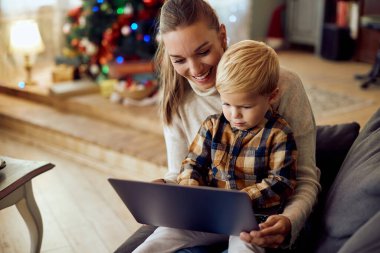 Small boy and his mother using laptop while relaxing at home on Christmas day.