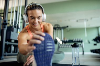 Smiling female athlete doing relaxation exercises and stretching her leg at health club. 
