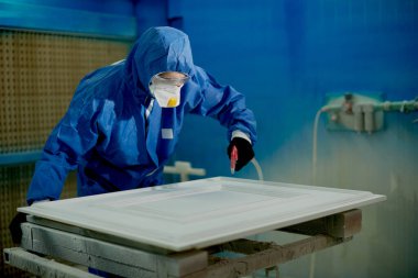 Male worker coloring processed timber with spray gun and woodworking factory. 