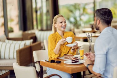 Happy couple communicating while enjoying in dessert and cup of coffee in a cafe. Focus is on woman. 