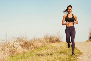 Full length of young smiling sportswoman running in nature. Copy space. clipart