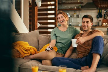 Young happy couple enjoying while watching something funny on a TV at home. 