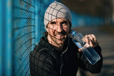 Happy athletic man refreshing himself and drinking fresh water while having sports training outdoors. 