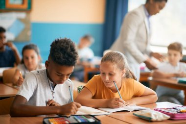 Smiling schoolgirl and her African American classmate studying during a class at elementary school. 