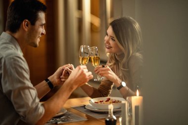 Young happy couple toasting with Champagne while holding hands and having dinner in dining room. Copy space. 