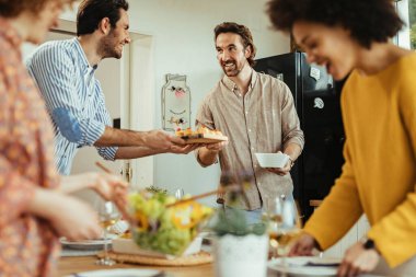 Young happy man and his friends enjoying while setting dining table for lunch at home. 