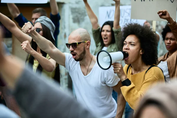 Young African American woman shouting through megaphone while participating in a protest for black civil rights. 