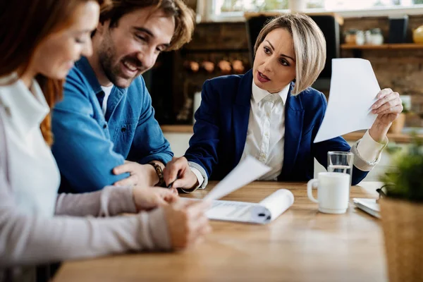 Insurance agent talking to young couple while analyzing document during a meeting at their home.