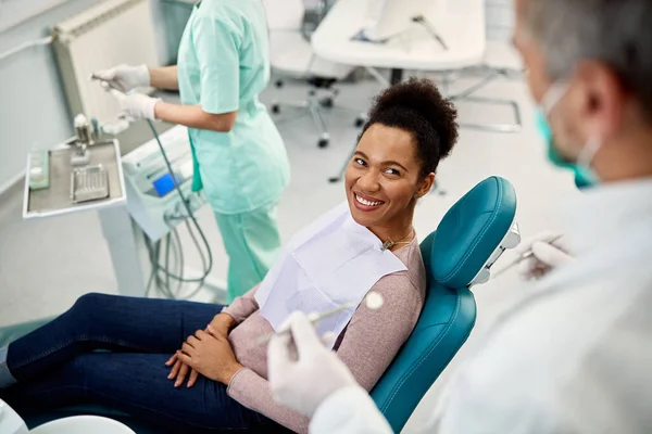Happy black woman talking to her dentist during dental exam at dentist's office.